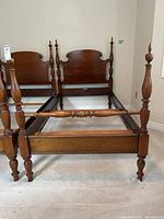 Full view of the wooden four poster bed frame with turned posts and finials. Visible scratches on wood surface.