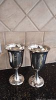 Two sterling goblets side by side on black countertop with tile backsplash