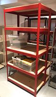 Full view of five-tier red metal shelving unit with particleboard shelves and some plastic storage bins on lower shelves.