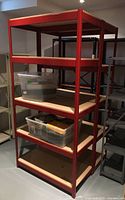 Full view of five-tier red metal utility shelving unit with pressboard shelves in basement storage area