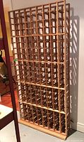 Front and angled views of the tall, wooden wine rack showing the grid-style slots for bottles and its wall-mounted suitability.