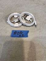 Two coiled Apple USB-C to USB-A cables with a handwritten label '#07 x2' on a blue piece of tape, placed on a gray surface.