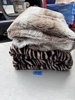 Photo showing two folded soft sofa blankets stacked: one cream-colored and one dark brown zebra-striped.