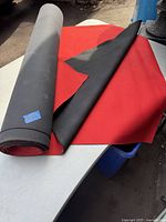 Long piece of fabric coated rubber unrolled on table showing red top surface and black textured underside.