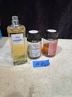 Photo showing three Chanel perfume items: one rectangular bottle with spray top and two smaller refill jars with liquid inside.