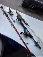 Three fishing rods on a table: red rod with red reel, white Shakespeare Navigator rod, and black rod with blue Herculy 98B reel.