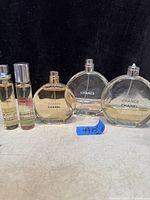 Photo of 5 Chanel Chance perfume bottles arranged in a row on a surface against a dark background. Two small spray bottles and three round bottles, one missing the spray nib.