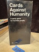 Photo of the Cards Against Humanity black box with white lettering and some colorful cards around it.