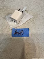 White Apple 20W USB-C power adapter in plastic sleeve on a gray surface with label '#08'.