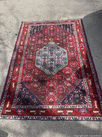Full view of the vintage Persian-style area rug laid flat on pavement showing overall condition, pattern, and colors.