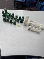 Photo showing all 32 chess pieces arranged in two groups by color on a table: 16 green onyx pieces and 16 white onyx pieces.