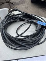 Coiled black extension cord approximately 50 feet long placed on a table, showing the thickness and coiling condition of the cord.