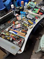 Full view of the assortment of tools and hardware on a table including a metal toolbox, hand tools, tape, and screwdrivers.
