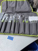 Overall view of Wolfgang Puck 8 piece kitchen prep set in a gray and green fabric roll-up pouch, all wrapped in plastic.