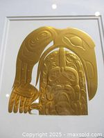 Close-up front view of gold high relief artwork depicting raven and salmon design.