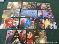 Set of eleven Star Trek themed First Day Cover envelopes arranged on green background, showing multiple series characters and related postmarks.