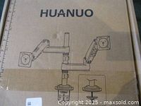 Brown cardboard box with black line drawings and HUANUO brand name on the front. Shows illustration of dual monitor arms and clamp base.
