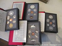 Four sets of Royal Canadian Mint coins in presentation folders containing various coin denominations arranged in black trays, displayed on a flat surface.