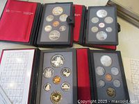 Four coin sets displayed in black and red folders with multiple coins visible within foam.