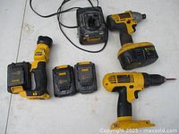 Photo showing two yellow and black DeWalt cordless drills, charger, two rechargeable batteries on white surface.