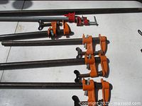 Overview photo showing five clamps and one extra long steel bar laid out on a flat surface.