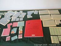 Red binder album and assorted mint stamp sheets arranged on green surface