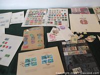 Wide view of multiple stamp sheets and FDCs arranged on green surface, showing various countries and themes.