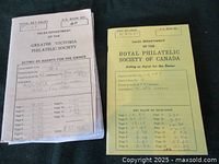 Photo showing the yellow and white front covers of two stamp books. The white booklet is from the Greater Victoria Philatelic Society with handwritten notes and printed form details. The yellow booklet is from the Royal Philatelic Society of Canada with similar details and catalog numbers.