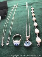 All jewelry items laid out on green fabric: two pearl necklaces, eyeball ring, eyeball pendant necklace, mother of pearl bracelet