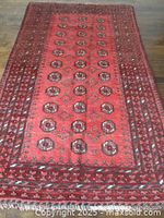 Front top view of a vintage Bokhara style area rug with repeating medallion patterns in deep red and dark accents on a wooden floor.
