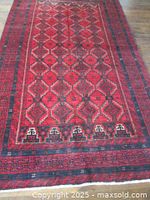 Full view of red wool rug showing geometric diamond pattern and dark border on hardwood floor