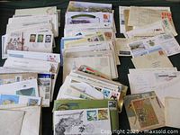 Full view of multiple stacks of First Day Covers arranged on a flat surface showing an assortment of envelopes with various stamps and commemorative prints.