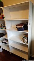 Front view of white melamine 5-shelf bookcase with some items on shelves for scale, mostly empty.