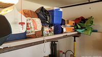 Shelf with multiple camping items including a white hard cooler, blue soft cooler, camping chairs, bags, and miscellaneous gear.