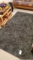 Gray shaggy carpet shown in a room with visible furniture around it, thick plush texture visible.