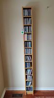 Photo of tall, narrow wooden CD rack filled with CDs, showing the overall storage and amount of CDs included.