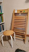 View showing one folding chair leaning against the wall and the small round stool with white metal legs in front.