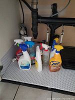 Various cleaning spray bottles with different trigger colors (blue, white, yellow) placed under a sink.