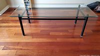 Full view of rectangular coffee table with metal base and glass top on hardwood floor.