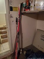 Full view of skis standing upright showing length and detail, taped to wall near stairs.