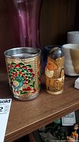 Colorful enamel peacock design cup and hand-painted wooden nesting doll on wooden shelf