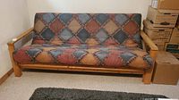 Front view of futon couch bed showing wooden frame and multicolored patchwork patterned cushion