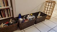 Three brown plastic baskets with household cleaning products and miscellaneous items, plus a wooden circular rack on the floor.