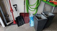 Wide view showing garden pots, shovels, broom, hose, washer fluid bottle and bag of material.