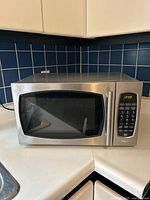 Front and right angled view of stainless steel Salton microwave showing the door, keypad, and current time on display.