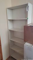 White shelving unit positioned next to a cardboard box, showing full front view of five shelves.