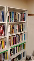 Front view of white shelving unit filled with numerous books showing the adjustable shelf spacing and overall condition.