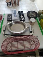 Photo showing three silver trays, a metal steamer basket, a wooden bowl, a red wire basket, a small candle, and a pot holder