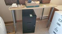 Full view of rectangular metal legged table with items on top and a black filing cabinet underneath.