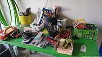 Wide view of table with assorted tools including staplers, wrenches, paint brushes, and baskets containing various small tools and hardware.